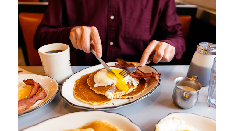 Man eating pancakes with fried egg and bacon at the diner, close-up