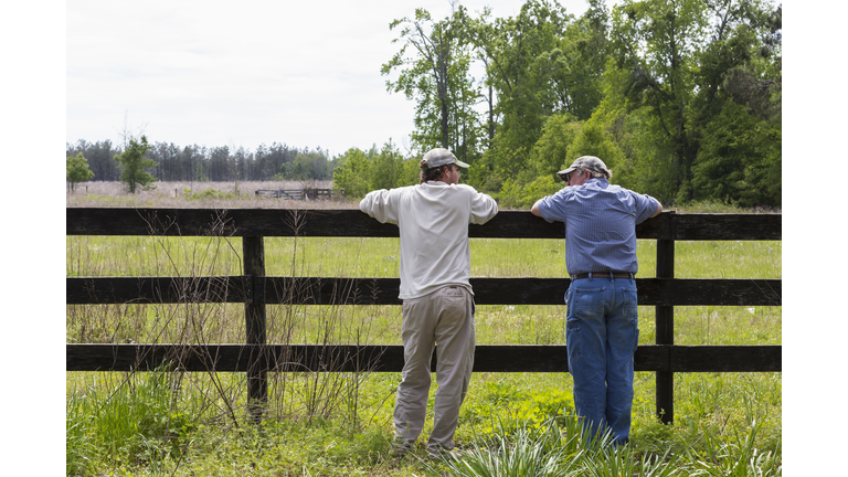 Caucasian father and son leaning on fence by rural field