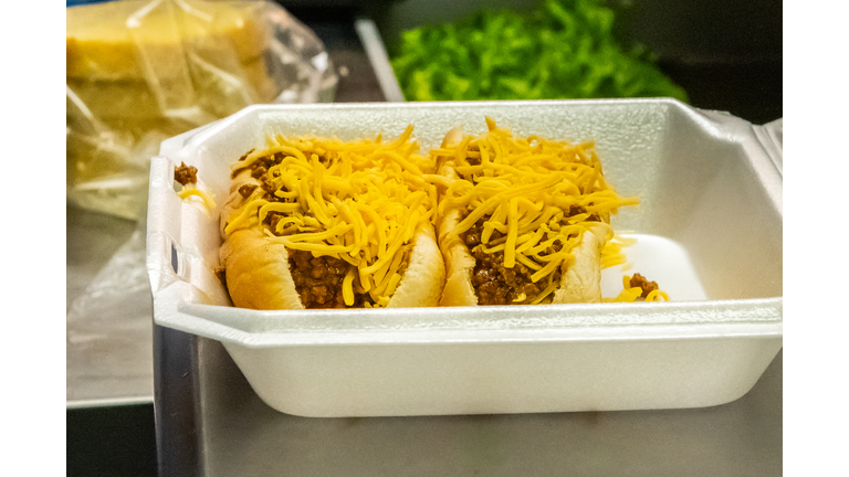 A close up of two chili cheese dogs in a diner to go container