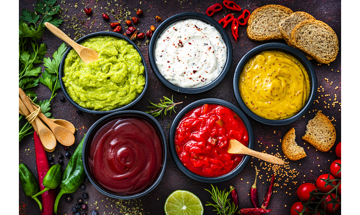 Set of five dip sauces shot from above on dark table