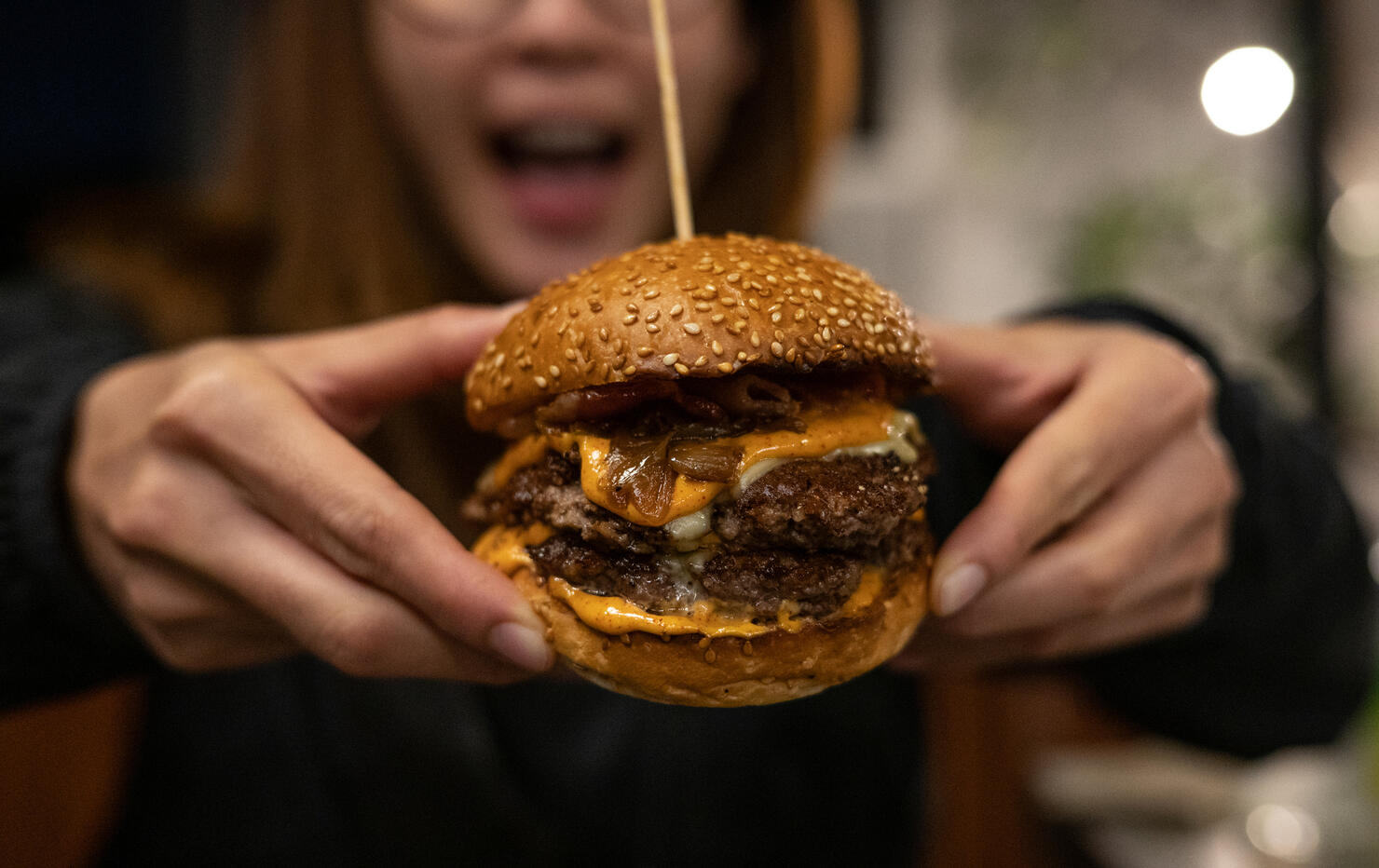 Close up of woman opened her mouth, ready to eat a double beef cheeseburger.