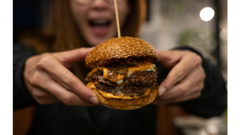 Close up of woman opened her mouth, ready to eat a double beef cheeseburger.