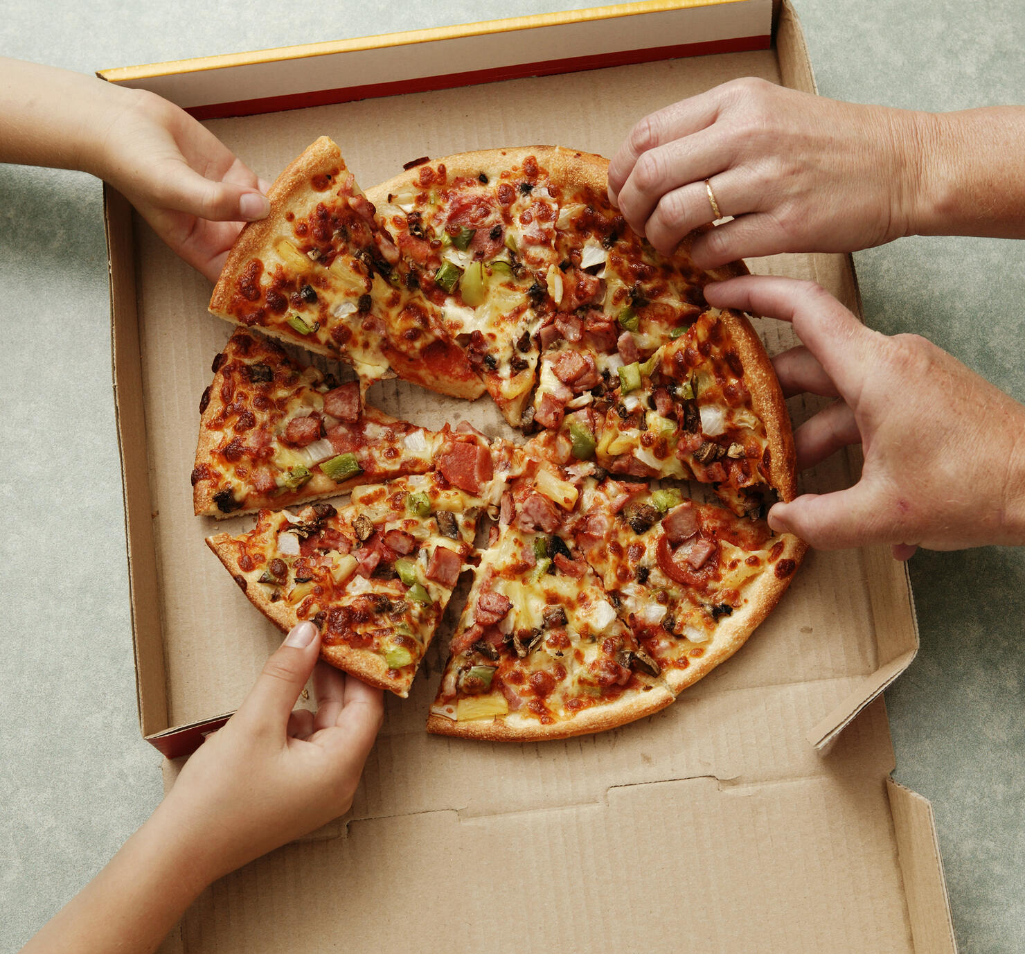 Family taking slices of pizza from pizza box, elevated view