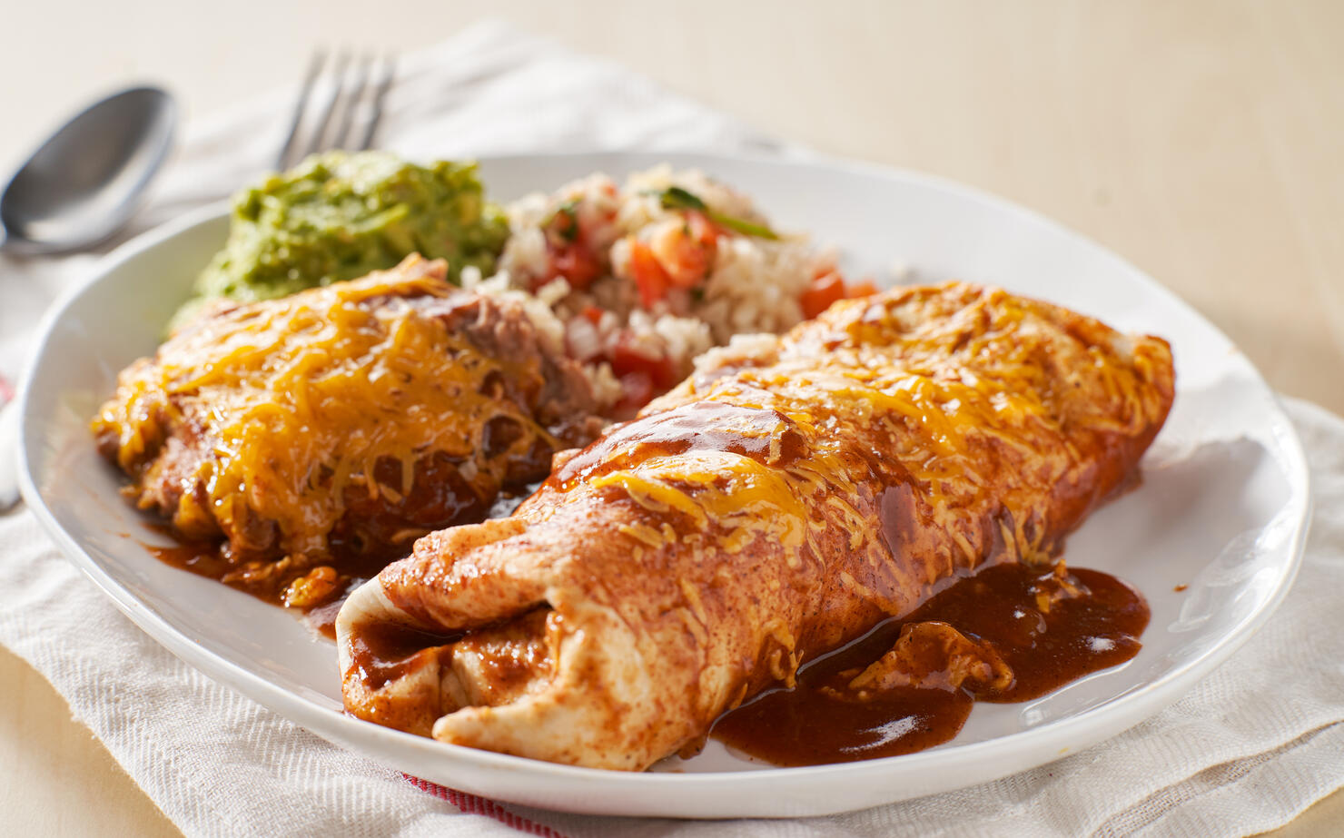 mexican wet burrtio platter with red enchilada sauce, refried beans, rice and guacamole