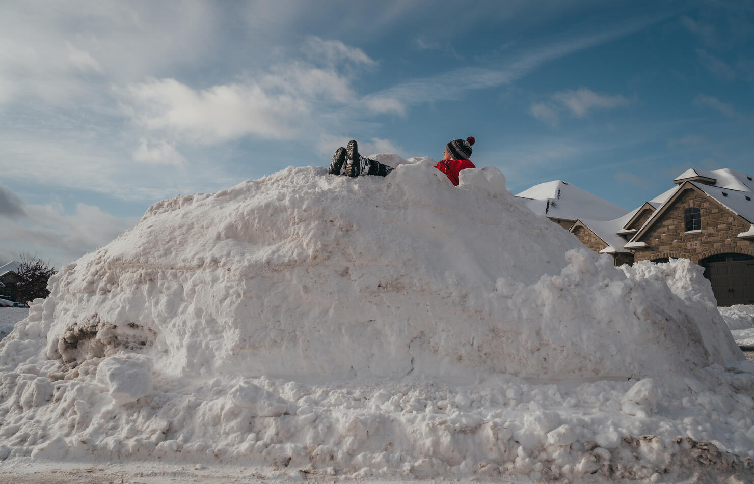 Young boy sitting on top of a big snow pile on winter day