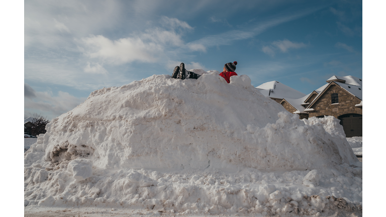 Young boy sitting on top of a big snow pile on winter day