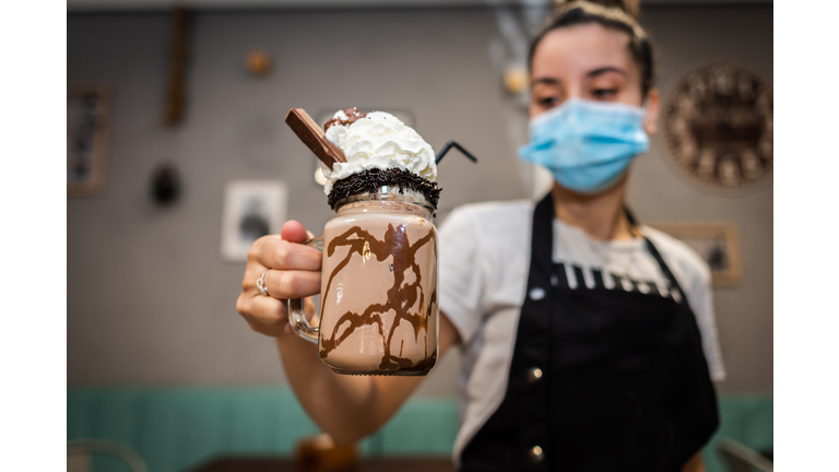 Waitress wearing face mask offering a chocolate milkshake