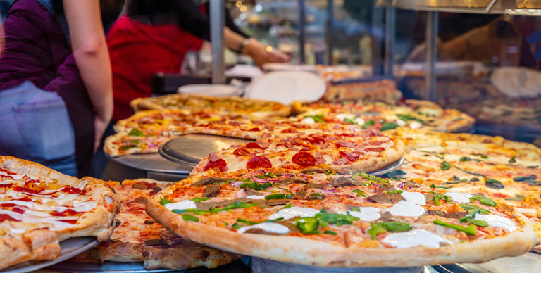 Assortment of italian pizzas in a shop display. Female workers serving the pizzas.