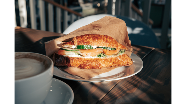 Fresh croissant with salmon slices, fresh cucumber and a cup of coffee for breakfast.