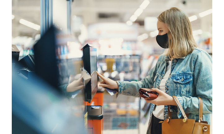 Woman in medical mask pays at self-checkouts.