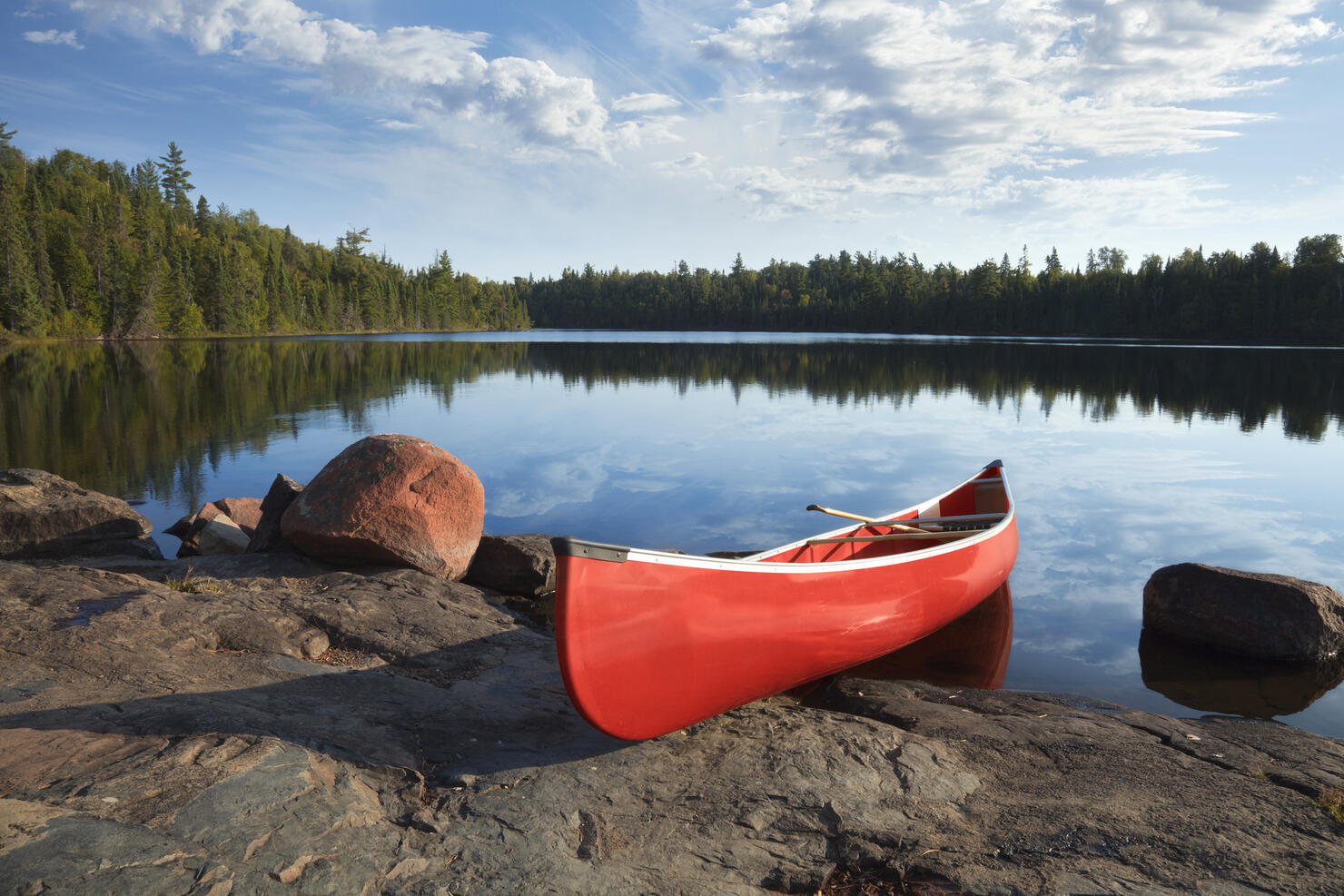 Red canoe on rocky shore of calm northern lake