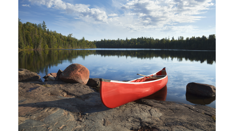 Red canoe on rocky shore of calm northern lake