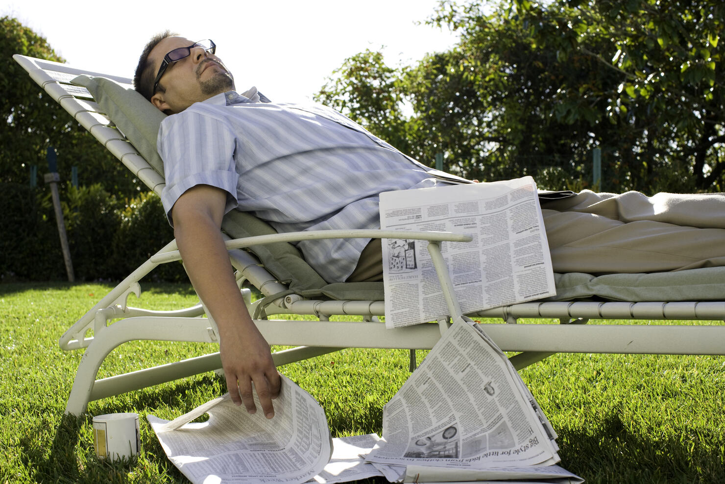 Man with newspaper asleep on garden loungechair