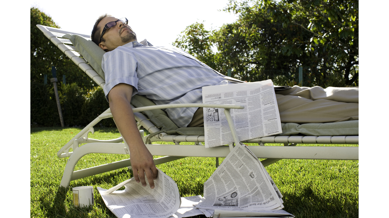 Man with newspaper asleep on garden loungechair