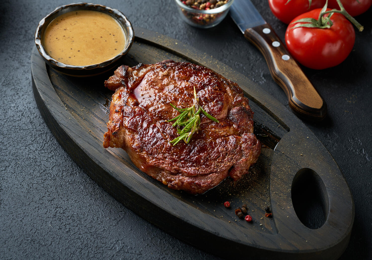 Fresh juicy delicious beef steak served on wooden cutting board over black background.