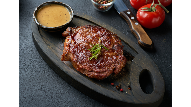 Fresh juicy delicious beef steak served on wooden cutting board over black background.