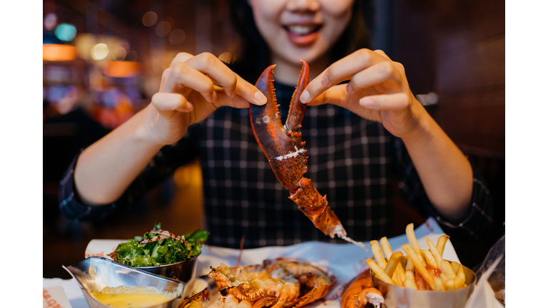 Smiling Asian woman holding a grilled lobster claw in restaurant
