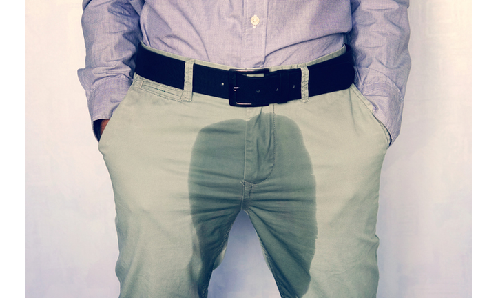 A man standing in wet pants against the wall. Urinary incontinence is an increasingly popular disease affecting younger males. incontinence and wet pants. a dark spot on a light trousers.