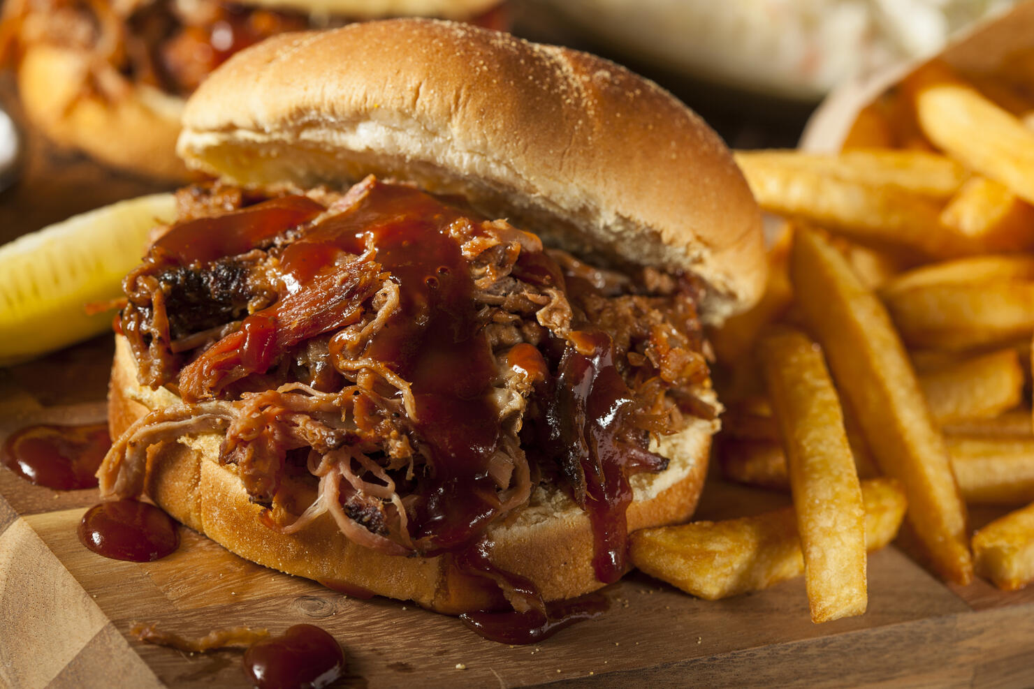 Barbeque pulled pork sandwich and fries on wooden board