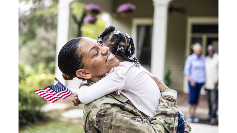 Daughter embracing female U.S. soldier mother in front of home