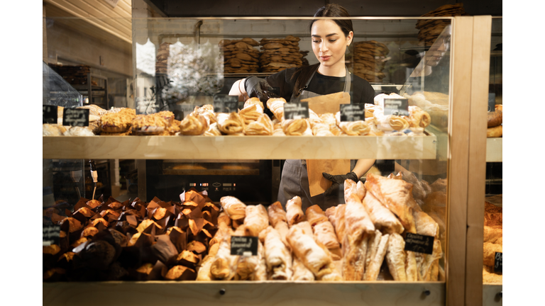Young woman preparing pastry for sale in supermarket bakery department. Bakery seller.