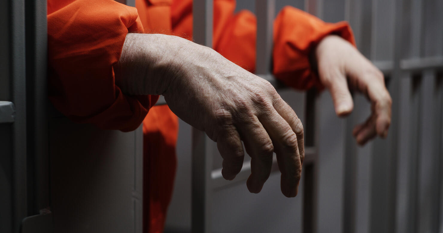 Hands close up of elderly prisoner holding metal bars