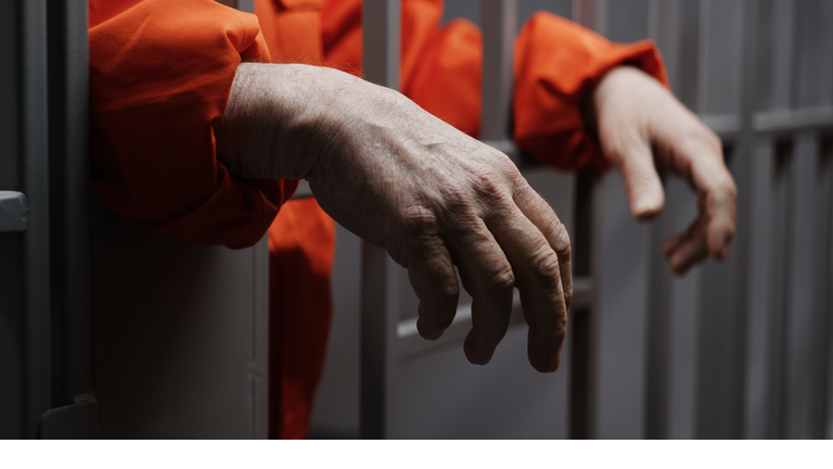 Hands close up of elderly prisoner holding metal bars