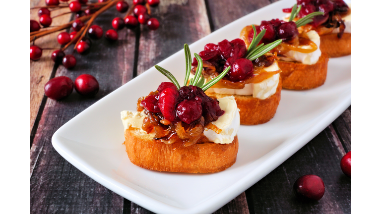 Crostini appetizers with cranberries, brie and caramelized onions on a plate against wood