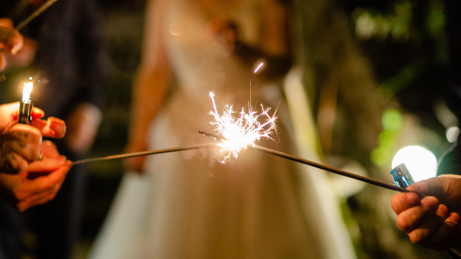 Sparklers used celebrating a wedding with the bride and groom stood out of focus in the background.