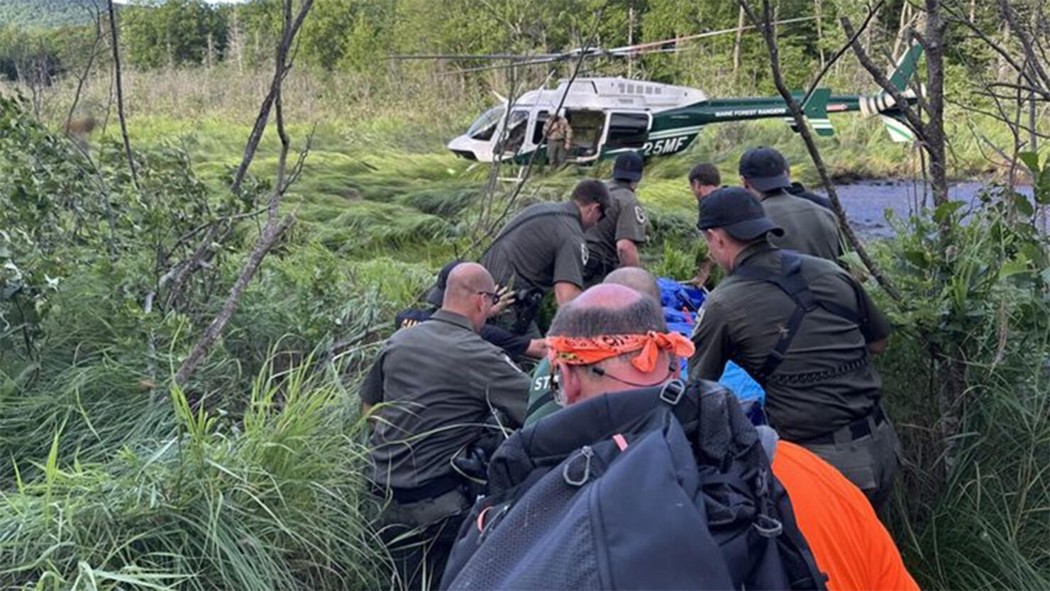 A team of rescuers carry a man to a helicopter.