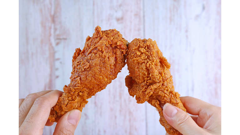 Closeup Man's Hand and Woman's Hand Clinking Crispy Fried Chicken Drumsticks Against Wooden Wall