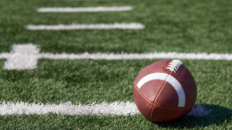 American football ball at yard line markers on playing field