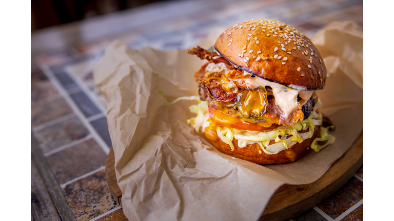 Bacon cheeseburger with salad in bun, served on wooden board