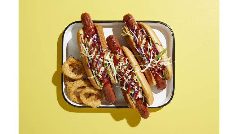 Three hotdogs on tray with onion rings, overhead view on yellow background