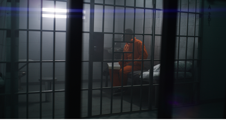 African American prisoner sits on the bed, reads Bible