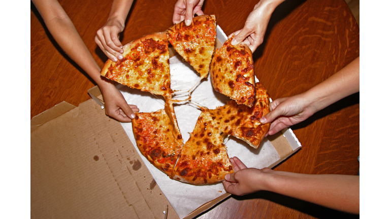 People grabbing slices of pizza, overhead view