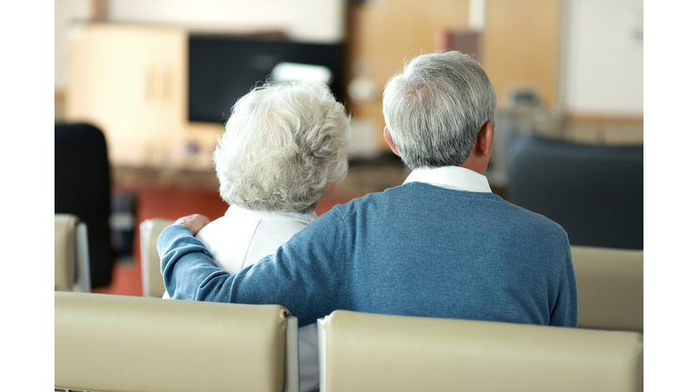 Rear view of senior couple sitting in hospital waiting room