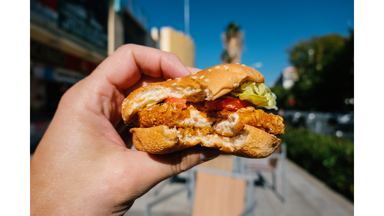 Close up view of man holding chicken burger, in background blurred image of city.