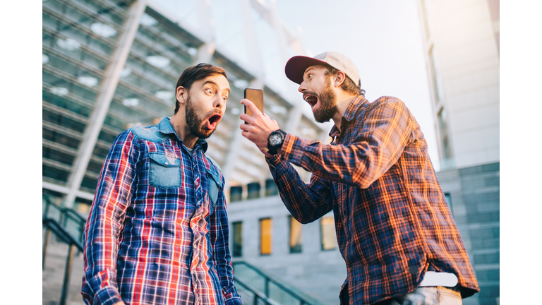 Men being happy winning a bet in online sport gambling application with football stadium on the background