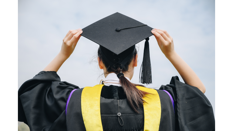 Rear view of young student wearing graduation gown with graduation cap in her commencement day.