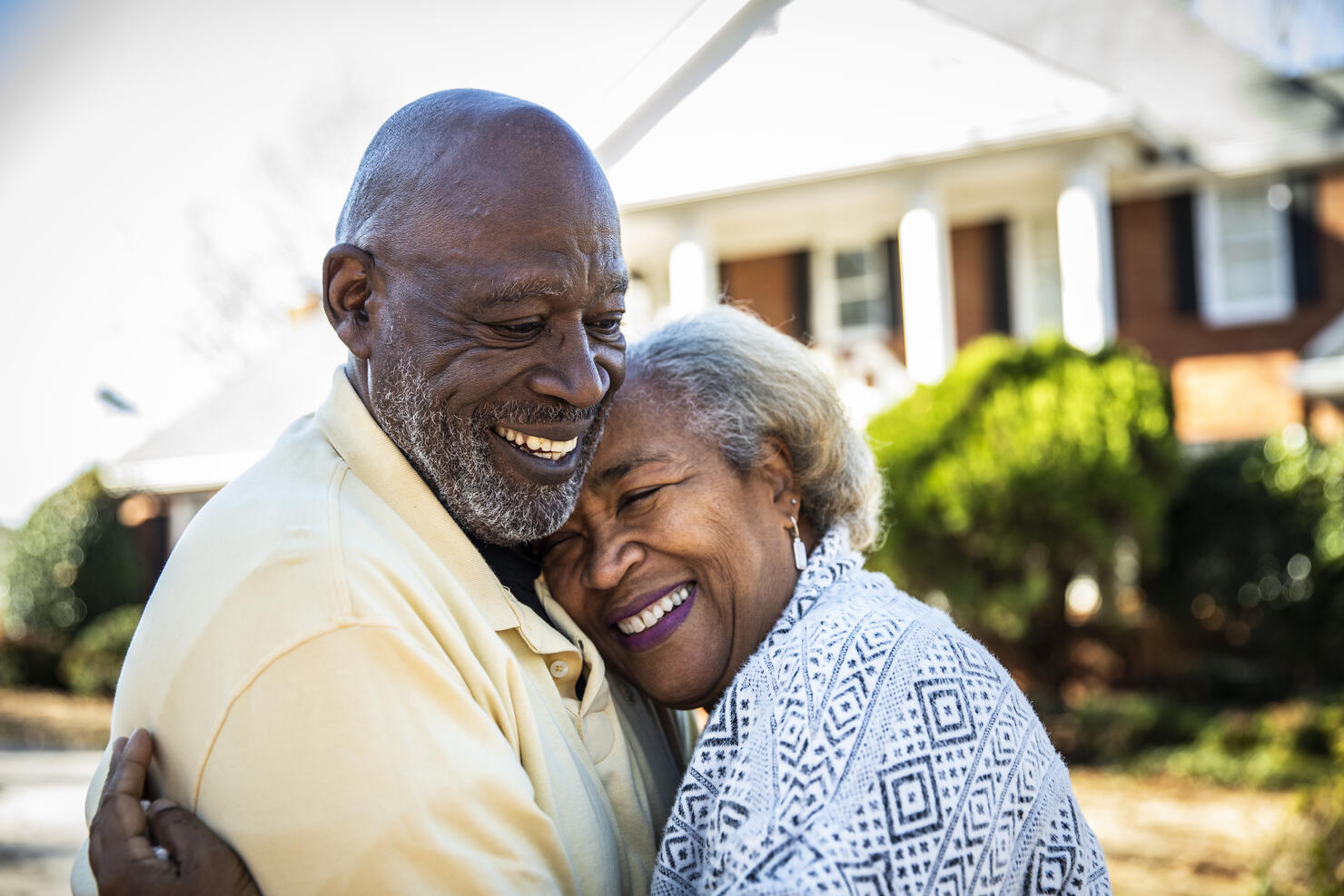 Senior couple embracing in front of residential home