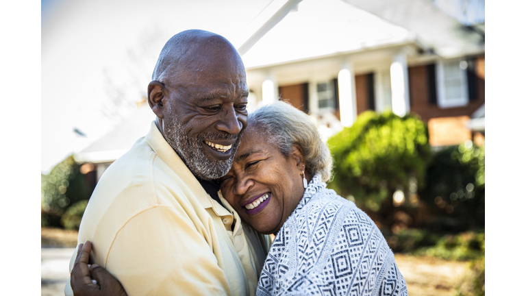 Senior couple embracing in front of residential home