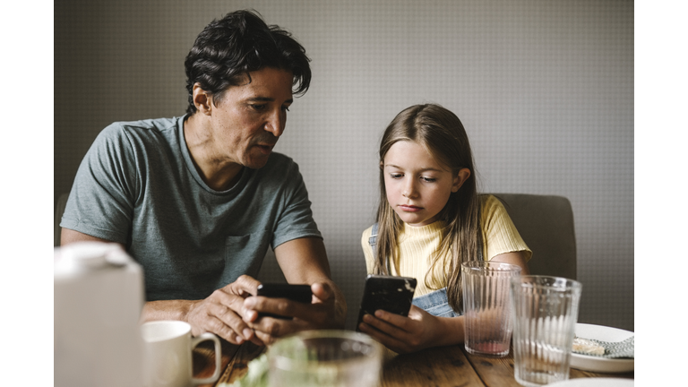 Daughter and father using smart phone over dining table at home