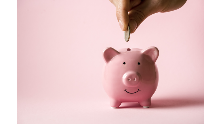 Hand puts a coin in a piggy bank.