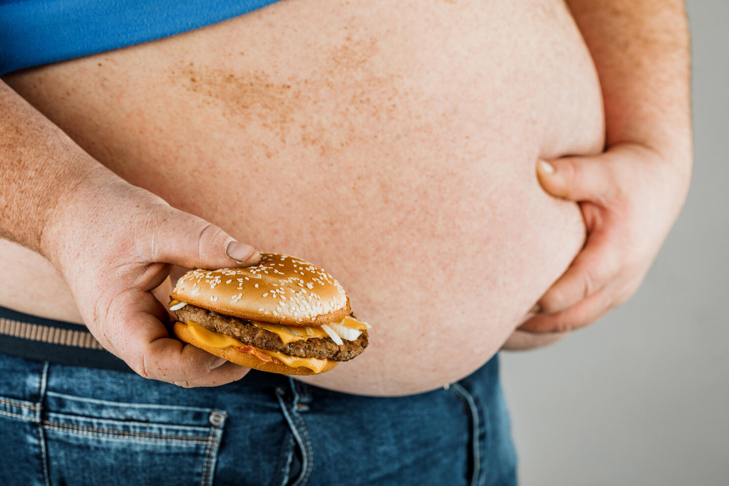 fat man with a hamburger in his hand on a gray background.