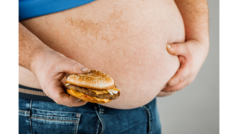 fat man with a hamburger in his hand on a gray background.