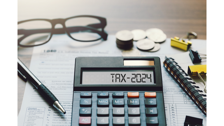 Word Tax 2024 on the calculator. Business and tax concept.Calculator, coins, book, tax form, and pen on table.Tax deduction planning.Financial research, government taxes, and calculation tax return