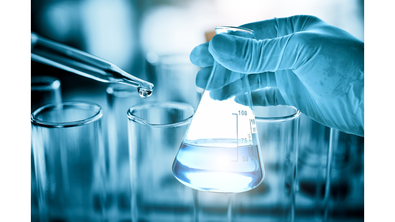 hand of scientist holding flask with lab glassware in chemical laboratory background, science laboratory research and development concept