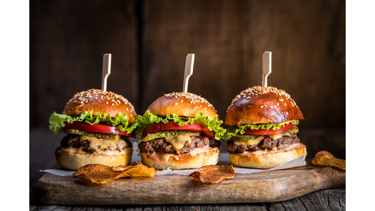 Tasty cheeseburger with lettuce, cheddar cheese, tomato and pickles. Burger bun with sesame seeds. Rustic atmosphere. Delicious fast food meal.