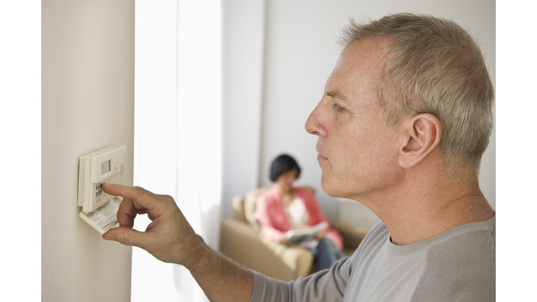 USA, New Jersey, Jersey City, Mature man adjusting room temperature, while woman is sitting in background